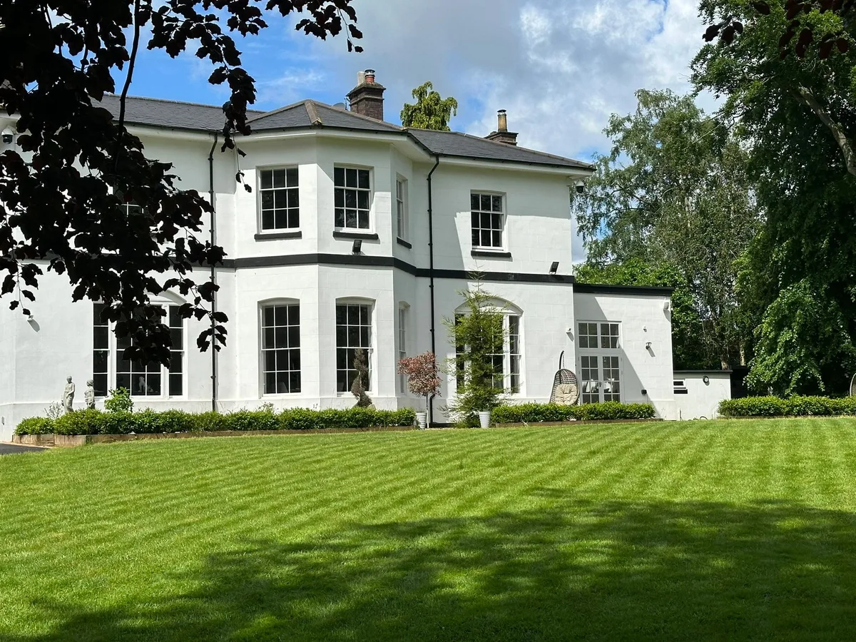 A carefully maintained lawn beside a white country house, surrounded by mature trees